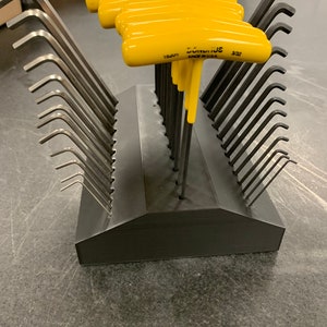May include: A set of 18 yellow and black L-shaped hex wrenches with a black plastic holder. The wrenches are arranged in a row and the holder is shaped like a house. The wrenches are labeled "BONDHUS 3/32 15007".