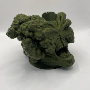 Puede incluir: Una escultura verde impresa en 3D de una criatura con una boca grande y muchos ojos. La escultura es detallada y texturizada, con una apariencia rugosa y org&aacute;nica.