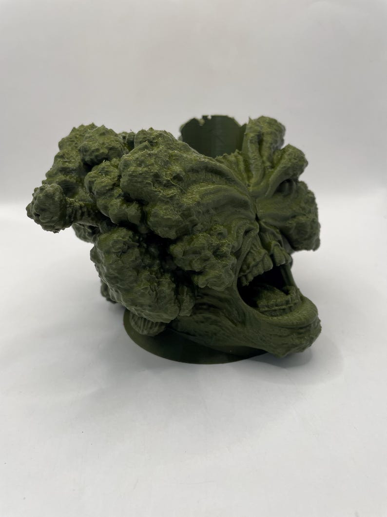 Puede incluir: Una escultura verde impresa en 3D de una criatura con una boca grande y muchos ojos. La escultura es detallada y texturizada, con una apariencia rugosa y org&aacute;nica.