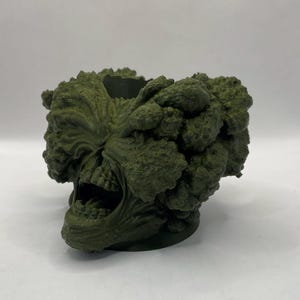 Puede incluir: Un macetero impreso en 3D con forma de cabeza de monstruo verde gritando con una superficie texturizada.