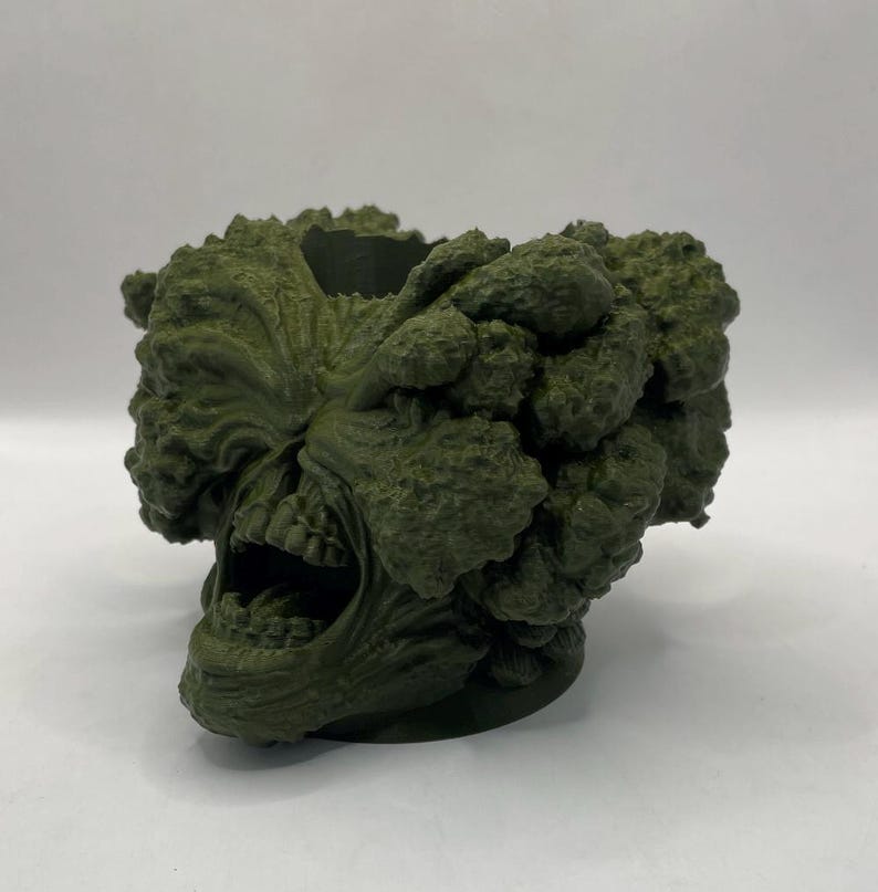 Puede incluir: Un macetero impreso en 3D con forma de cabeza de monstruo verde gritando con una superficie texturizada.