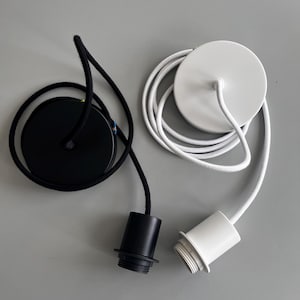 May include: Two pendant light fixtures, one black and one white. Each fixture has a circular ceiling plate and a cylindrical socket. The black fixture has a black cord, and the white fixture has a white cord.