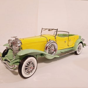 May include: A yellow and green vintage car model with chrome accents. The car has a convertible top and a spare tire on the back.