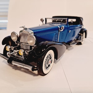 May include: A blue and black vintage car model with chrome accents and a detailed interior. The car has a black convertible top and a whitewall tire.