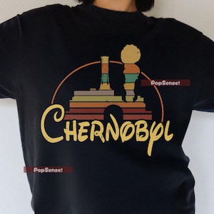 Könnte beinhalten: Schwarzes T-Shirt mit einer Retro-Grafik eines Atomkraftwerks mit dem Text "Tschernobyl" in einer stilisierten Schrift.