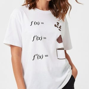 May include: A white short-sleeved t-shirt featuring a mathematical derivative sequence printed in black. The graphic shows f(x) equals coffee beans, f'(x) equals coffee grounds, and f''(x) equals a full cup of black coffee.