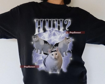 Könnte beinhalten: Schwarzes T-Shirt mit einem Grafikdesign mit drei Katzen und dem Wort "HUH?" in einer stilisierten Schriftart. Das Design beinhaltet einen lila Blitzeffekt und den Text "PopSense!" auf dem Shirt.