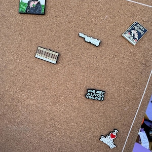 Puede incluir: Una colección de pines esmaltados con escenas y citas de la novela "Orgullo y Prejuicio". Los pines incluyen una pareja abrazándose, una portada de libro y frases como "We are all fools in love."