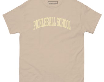 Może przedstawiać: Beżowa koszulka z napisem "Pickleball School" w żółtym łuku na przodzie.