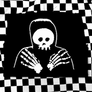 May include: Black patch featuring a white illustration of a hooded figure with a skull face and skeletal hands. The patch is on a black background and is surrounded by a black and white checkered pattern.