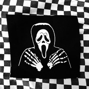 Könnte beinhalten: Schwarz-weißes Bügeleisen-Patch mit einem Geist, der eine weiße Maske mit einem schreienden Gesicht und Skeletthänden trägt.