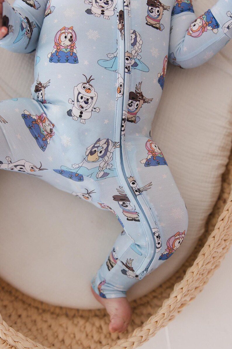 May include: Light blue baby sleeper featuring a repeating pattern of cartoon characters and snowflakes. The one-piece garment has a full-length zipper and long sleeves. The sleeper is made of a soft material and is designed for comfort.