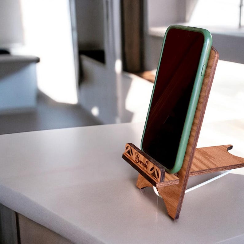 May include: A wooden phone stand with the name "Sarah" engraved on it. A green phone is resting in the stand.