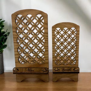 May include: Two wooden phone stands with a decorative lattice design. The larger stand is labeled "Alice" and the smaller stand is labeled "Sarah".