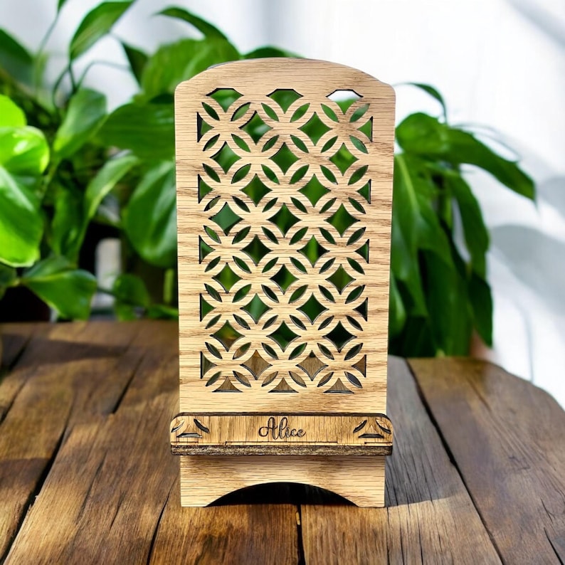 May include: A wooden phone stand with a geometric design and the name "Alice" engraved on the front. The stand is made of light brown wood and has a rustic look.