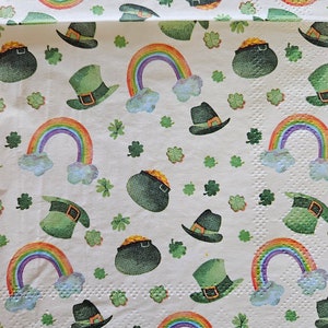 May include: White paper napkin with a repeating pattern of green shamrocks, rainbows, leprechaun hats, and pots of gold.