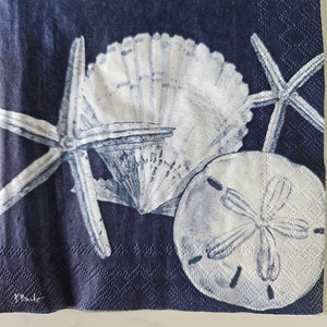 May include: A navy blue fabric napkin with a white seashell, two white starfish, and a white sand dollar. The napkin has a textured surface.
