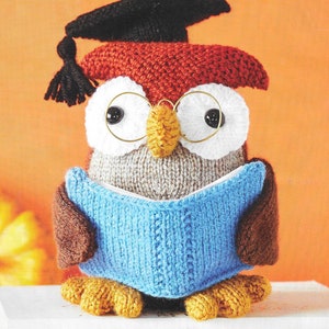 Peut inclure: Un hibou en tricot portant un bonnet de graduation et des lunettes, tenant un livre bleu. Le hibou est brun, gris et orange.