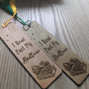 May include: Two wooden bookmarks with the text "I Read Past My Bedtime" and a book illustration. One is light brown, the other darker. Each has a tassel with green and yellow threads.
