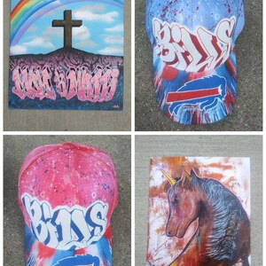 May include: Four different pieces of art, including a painting of a rainbow with a cross, a painting of a unicorn, and two baseball caps with the word "Bills" painted on them.