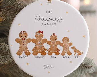 May include: White ceramic Christmas ornament with a gingerbread family illustration. The ornament features a gingerbread dad, mom, two girls, a boy, and a dog. The text "The Davies Family" and "2024" are printed on the ornament.