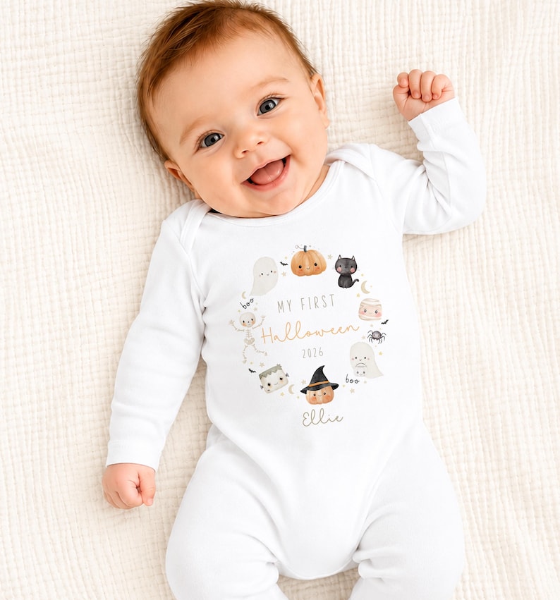 May include: A white long-sleeve baby bodysuit featuring a central graphic of a wreath made of small Halloween characters including a pumpkin, ghost, black cat, skeleton, and witch hat. The text reads My First Halloween 2026 and the name Ellie.