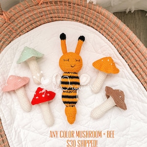 May include: A collection of five crocheted items including a central orange and black striped bee with antennae and four mushrooms in light green, pink, red, and orange with white spots. The text reads ANY COLOR MUSHROOM + BEE $30 SHIPPED!