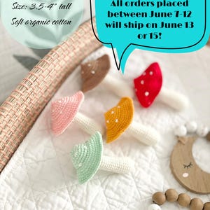 May include: Five crocheted mushroom rattles in brown, red, pink, yellow, and light green, each with a cream-coloured stem and white dots on the cap. Text reads: Mushroom rattle, Size: 3.5-4" tall, Soft organic cotton, Shop on vacation!