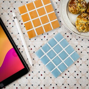 May include: Two ceramic tile samples, one orange and one light blue, with a grid pattern. The tiles are on a white background with a red and white polka dot pattern.