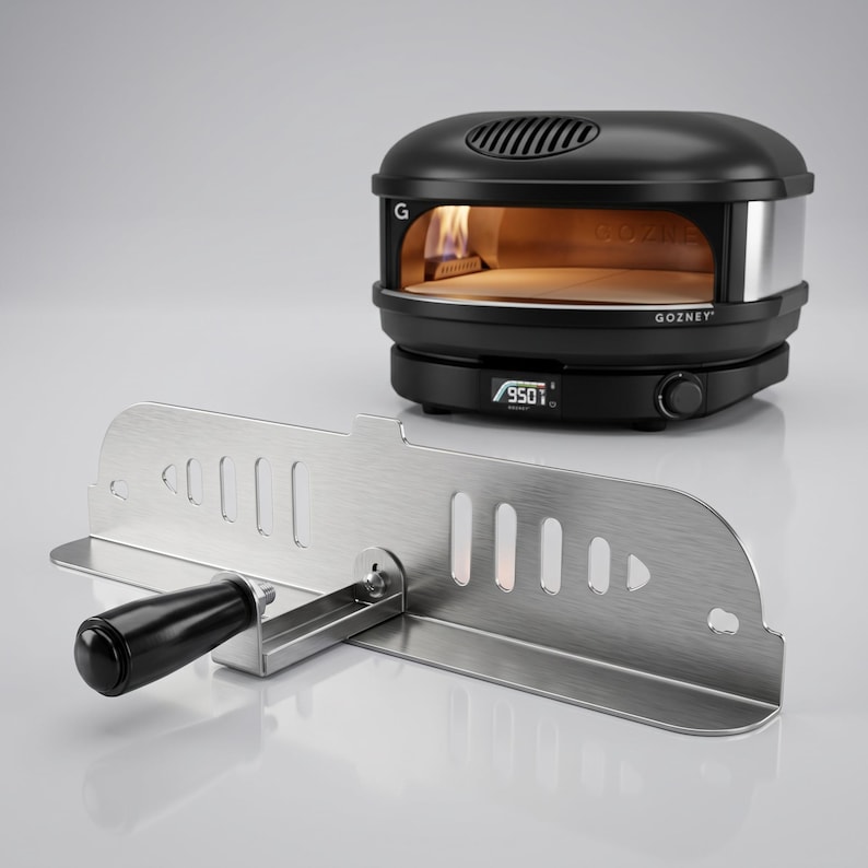 May include: Black and silver outdoor pizza oven with a stainless steel peel. The oven has a digital display showing 950 degrees. The oven has the brand name "Gozney" on the front.