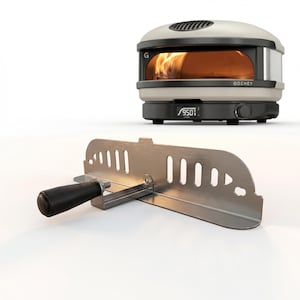 May include: A white and black outdoor pizza oven with a visible flame inside. The oven has the word "GOZNEY" on the front. A stainless steel pizza peel with a black handle is in the foreground.