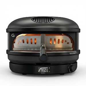 May include: Black outdoor pizza oven with the brand name "GOZNEY" visible. The oven features a digital temperature display showing 950 degrees Fahrenheit. The interior is lit with a warm glow, and a metal pizza peel is partially inserted.