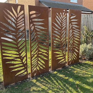May include: Four rectangular, weathered metal garden screens with a leaf design cut out. The screens are a rusty brown colour and stand upright in a grassy garden. The leaf pattern creates a decorative and natural look for outdoor spaces.