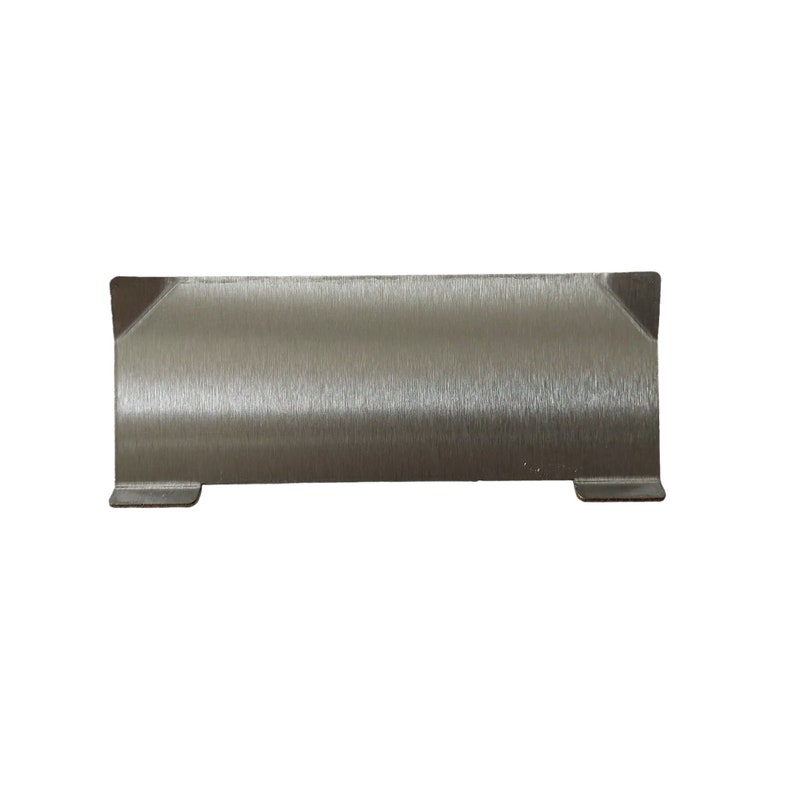 Puede incluir: Un objeto rectangular de metal cepillado con orientaci&oacute;n horizontal. El objeto tiene una superficie plana y texturizada y peque&ntilde;as extensiones anguladas en cada extremo. La parte inferior tiene dos peque&ntilde;os pies rectangulares. El objeto es de color plata neutro.