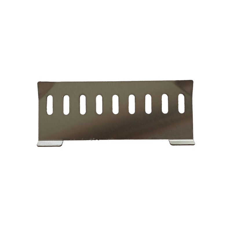 Puede incluir: Una cubierta de ventilaci&oacute;n de metal de acero inoxidable con forma rectangular y una serie de cortes ovales verticales espaciados uniformemente. La cubierta tiene dos peque&ntilde;os pies rectangulares en la parte inferior.