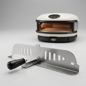 May include: A cream-colored pizza oven with a black base and the word "GOZNEY" printed on the front. A stainless steel pizza peel with a black handle is in the foreground. The oven has a digital display showing the temperature.