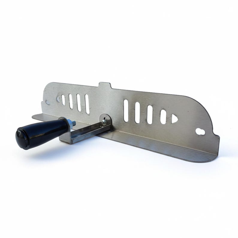 May include: A stainless steel tool with a black handle. The tool has a rectangular shape with several vertical slots and a curved edge. A handle is attached to the side with a bolt.