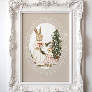 May include: A framed illustration of two bunnies decorating a Christmas tree. The bunnies are wearing dresses and holding a garland. The background is a light brown color.