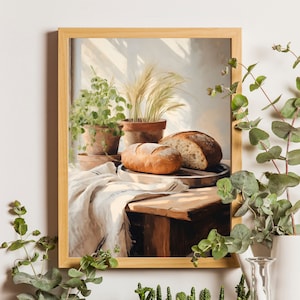 Könnte beinhalten: Ein gerahmtes Gemälde mit einer Stillleben-Darstellung von zwei Broten, einem weißen Tuch und Topfpflanzen. Das Brot liegt auf einem Holztisch mit braunem Hintergrund.