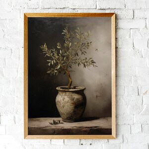May include: A framed art print depicting an olive tree in a pot. The tree has delicate branches and small green leaves. The pot is a weathered, light-coloured ceramic. The background has a gradient of dark and light tones.