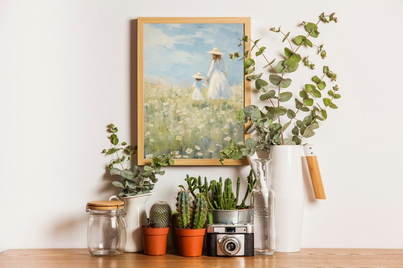 Peut inclure: Une peinture encadr&eacute;e repr&eacute;sentant deux personnes marchant dans un champ de fleurs blanches, un pichet en c&eacute;ramique blanche avec une poign&eacute;e en bois, un bocal en verre, une bouteille en verre transparent et quatre cactus en pot sur une surface en bois.