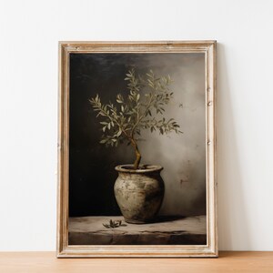 May include: A framed vintage print depicting an olive tree in a pot. The artwork has a muted colour palette and a weathered, antique aesthetic. The olive tree is in a rustic, textured pot, set against a neutral background.