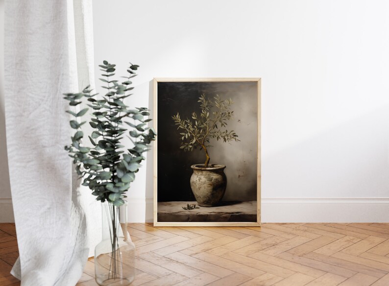 May include: A framed print of an olive tree in a pot, with a vintage feel. The artwork uses a muted colour scheme. The olive tree is in a rustic pot, set against a dark background. The frame is a light wood colour.
