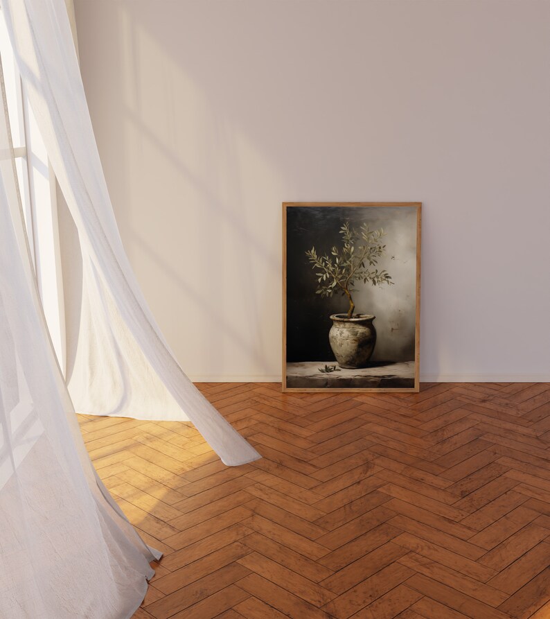 May include: A framed print depicting an olive tree in a weathered pot. The artwork is set against a dark backdrop, within a wooden frame. The image rests on a wooden floor, with white curtains in the foreground.