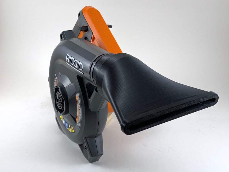Puede incluir: Un soplador de hojas de mano negro y naranja con una boquilla larga y negra. El soplador tiene la palabra "RIDGID" impresa en el lateral.