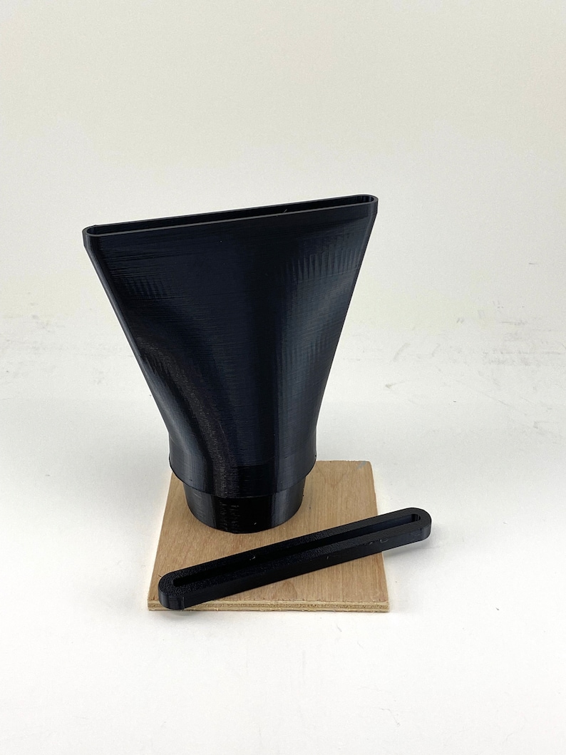 Puede incluir: Un embudo negro impreso en 3D con una abertura rectangular y una base redonda, sentado sobre una base de madera con una varilla negra impresa en 3D.