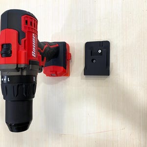 May include: A red and black Bauer cordless drill with a black battery and a black battery holder. The drill is mounted on a light wood surface.
