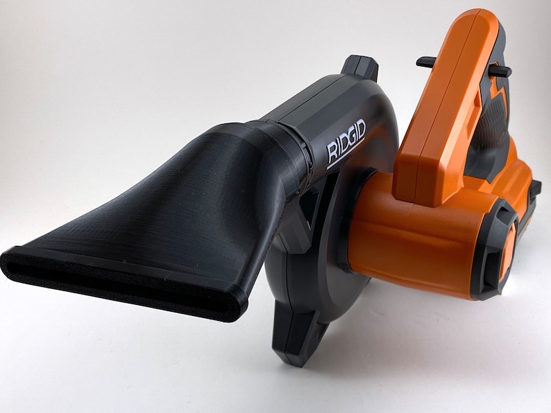 Puede incluir: Un soplador de hojas de mano negro y naranja con una boquilla larga y negra. El soplador tiene la palabra "RIDGID" impresa en el lateral.
