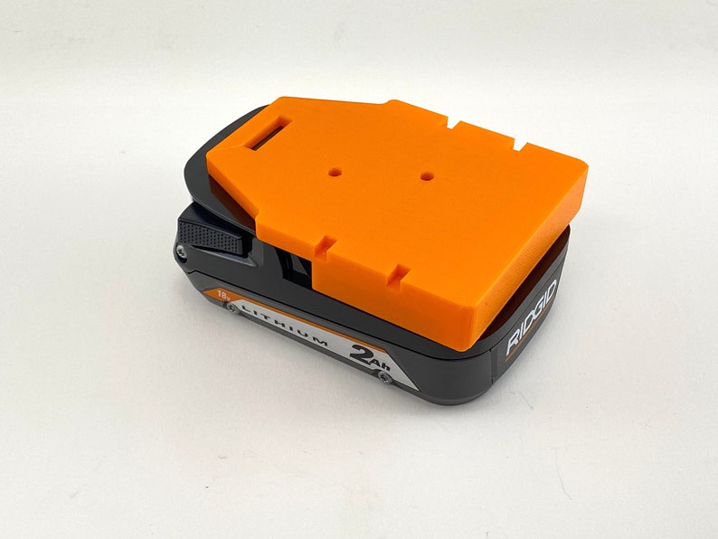 Puede incluir: Una bater&iacute;a de litio Ridgid de 18V 2Ah negra y naranja con una cubierta protectora naranja.