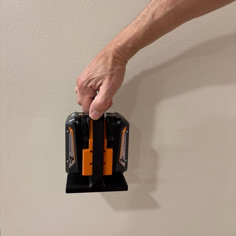 May include: Black and orange power tool battery charger with two battery slots. The charger has a black handle and base. The batteries are labeled "LITHIUM" and "2 Ah".